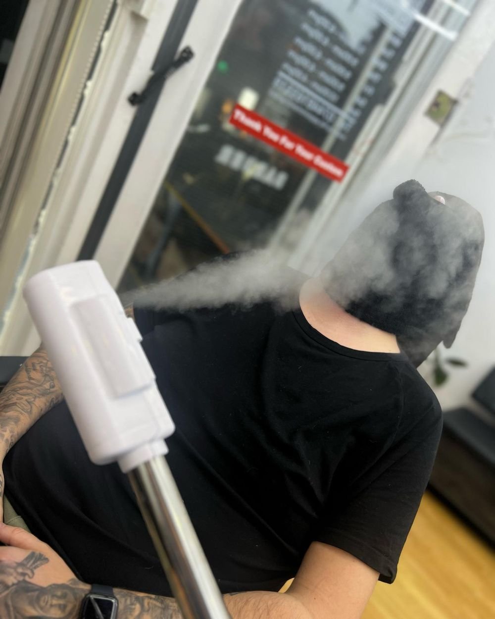 Steam rising over a client in a black-and-gold cape before a hot towel